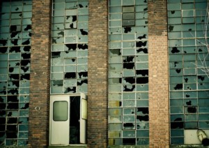 A brick building with tall, broken seal windows and a partially open white door at the bottom center.