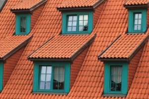 Close-up of a sloped roof with orange terracotta tiles, green-framed dormer windows, and well-maintained gutters—perfect for showcasing the importance of regular gutter cleaning.