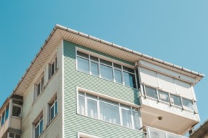 A multi-story residential building with light green and white siding, large windows, and a sloped roof rises against a clear blue sky—an ideal candidate for regular gutter cleaning frequency to maintain its pristine appearance.