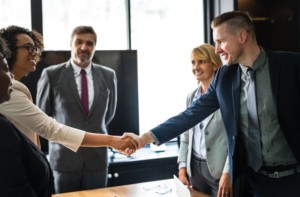 Two people in business attire shake hands across a table, while three colleagues look on—showcasing a successful meeting with an ideal client in a modern office setting.