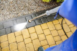 A person uses a pressure washer to clean yellow paving stones, removing dirt and grime and revealing the original color.
