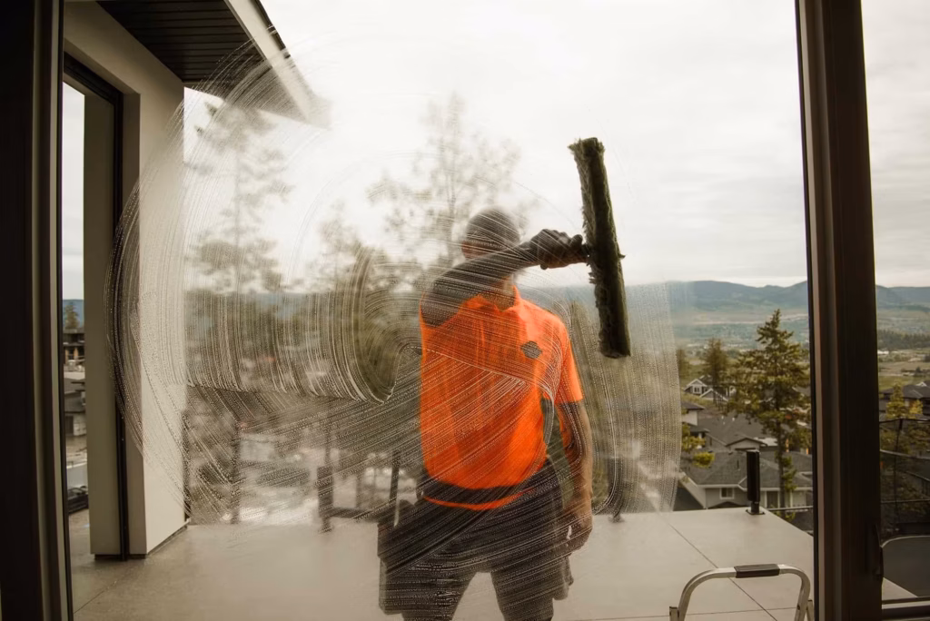 Live Next Level technician squeegeeing a large window, seen from inside the home