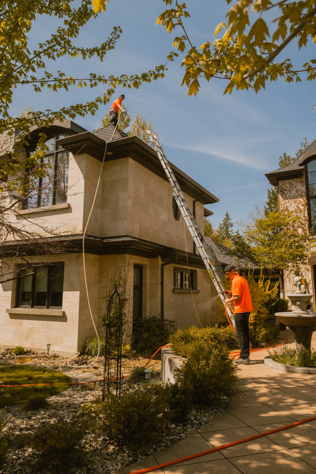 Live Next Level technicians working from a ladder and the roof edge on a two-storey Kelowna home