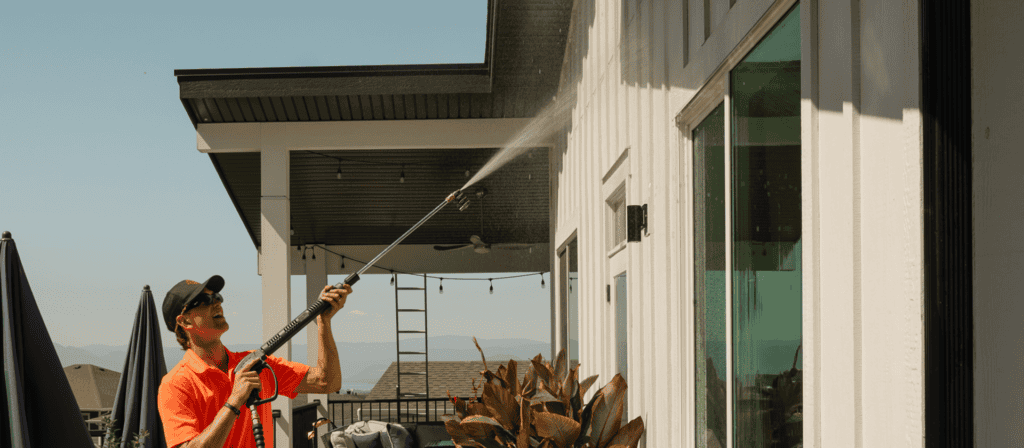 Technician soft washing the siding of a modern home