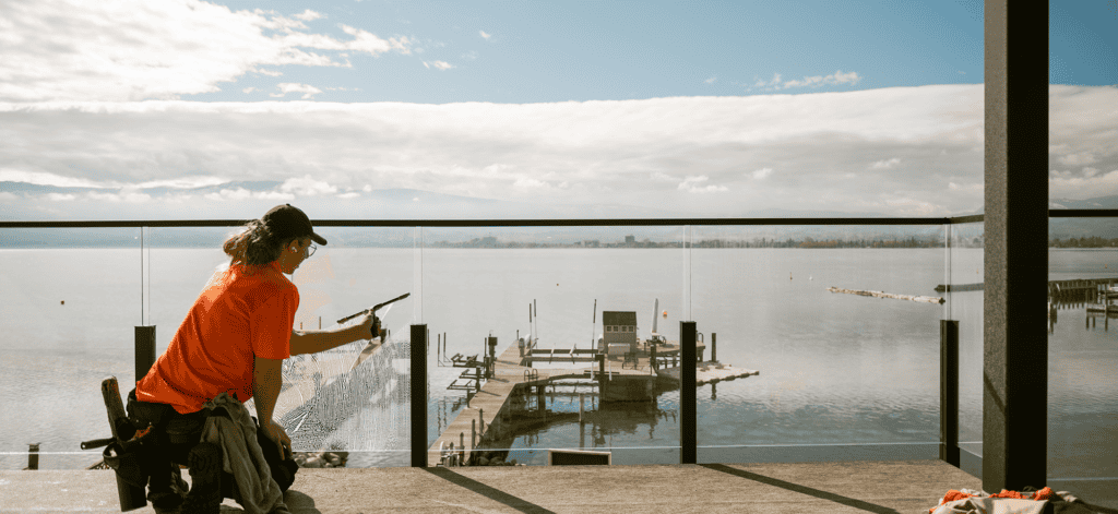 Technician cleaning glass balcony panels on a lakeside deck