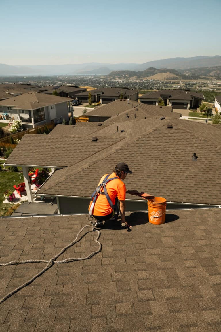Technician in a safety harness clearing gutter debris on a Kelowna roof