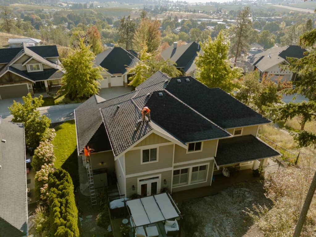 Aerial view of Live Next Level technicians treating moss on the asphalt shingle roof of a Kelowna home