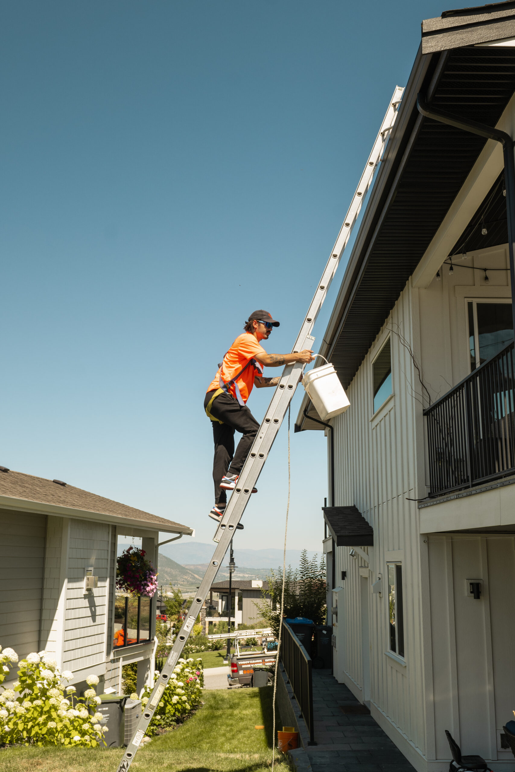 Technician accessing gutters by ladder on a multi-unit strata-style building