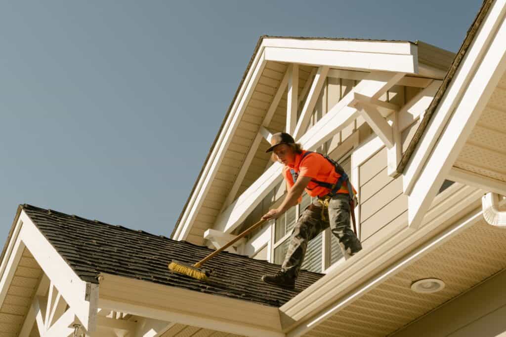 Live Next Level technician gently brooming loose moss down an asphalt shingle roof