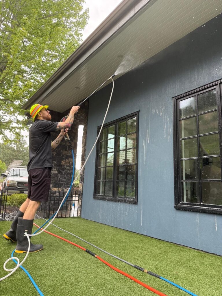 Technician rinsing the soffits and stucco of a Kelowna home after a soft wash